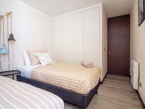 Un dormitorio con cama, mesita de noche, armario y una puerta que da a otra habitación.