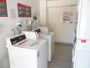 Een wasserette met twee wasmachines, een bedieningspaneel en informatieposters op de muren.