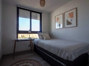 Een slaapkamer met een bed, een raam, een bureau en twee ingelijste kunstwerken aan de muur.