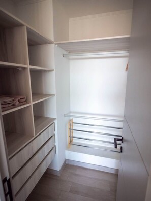 Et walk-in closet med åbne hylder, en bøjlestang og trægulv.