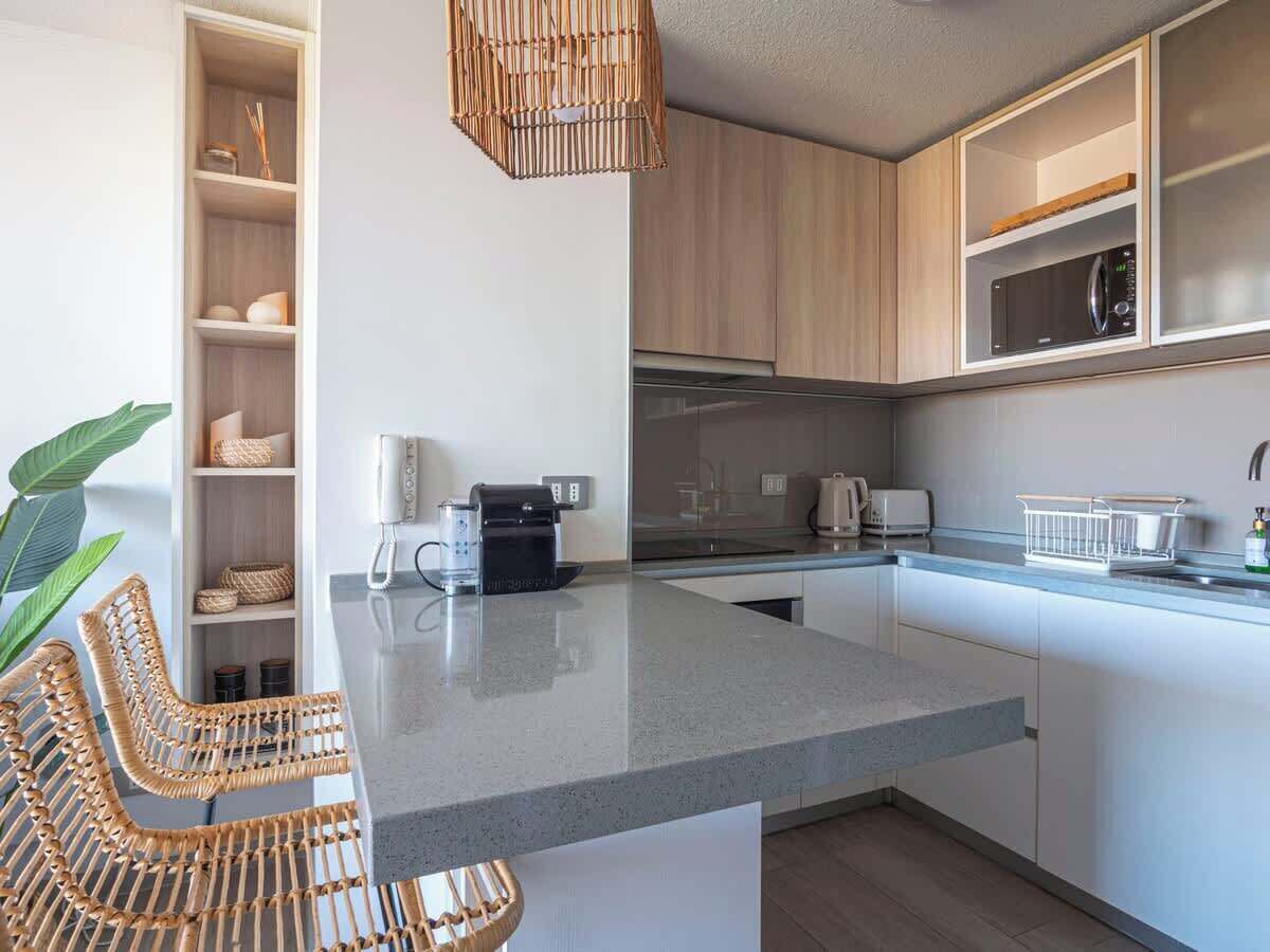 A modern kitchen with a granite countertop, built-in appliances, wicker chairs, and a hanging light fixture.