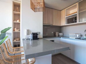 Et moderne køkken med en granitbordplade, integrerede hårde hvidevarer, fletstole og en hængende lampe.