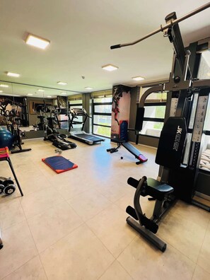 Et fitnesscenter med forskellig træningsudstyr, herunder løbebånd, vægte og en bænk.