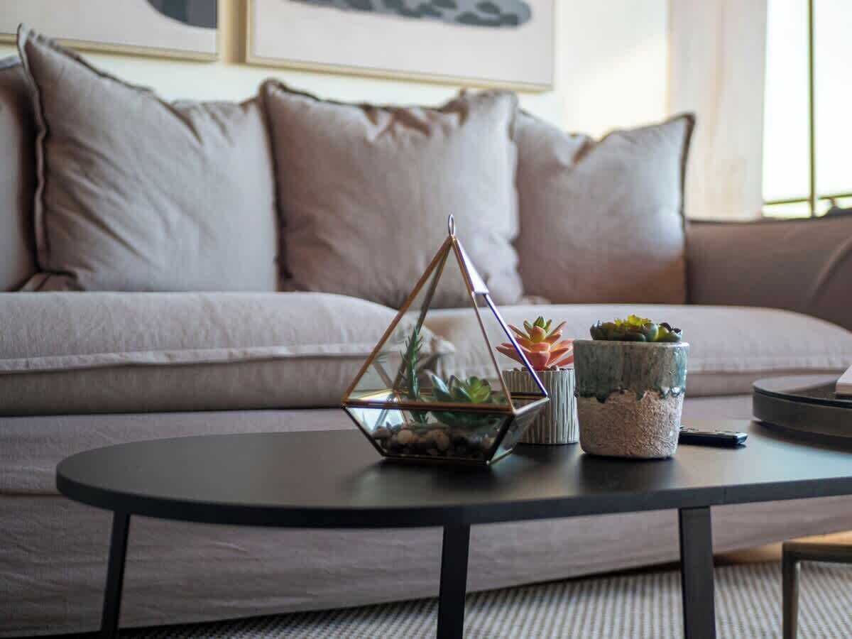 Een moderne woonkamer met een bank, een ronde salontafel en decoratieve plantenpotten.