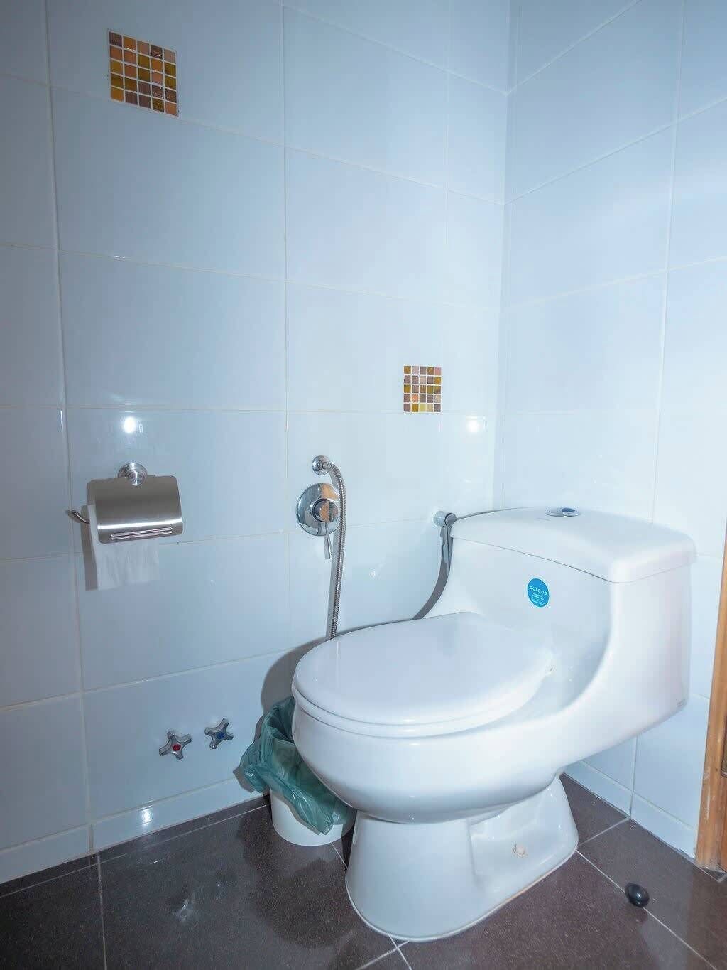 A bathroom with a toilet, a paper towel dispenser, and a shower head.