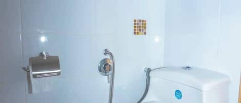 A bathroom with a toilet, a paper towel dispenser, and a shower head.