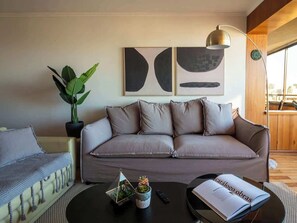 Ein modernes Wohnzimmer mit einer Couch, einem Couchtisch mit Dekoration, einer Topfpflanze und abstrakter Wandkunst.
