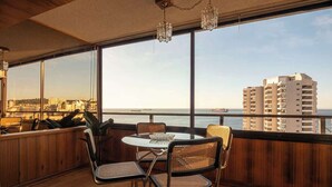 En balkong med ett bord och stolar, med utsikt över stadsbilden och havet.