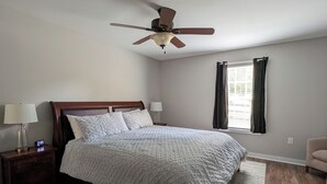 Een slaapkamer met een bed, nachtkastjes, een plafondventilator, een raam met gordijnen en een houten vloer.