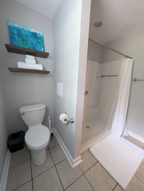 Ein Badezimmer mit Toilette, einer Duschkabine mit Glastür, einem Handtuchhalter und einem Bild an der Wand.