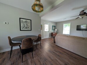 Ein geräumiger Wohnbereich mit Esstisch, Stühlen, einer Couch, einem Fernseher und einem Deckenventilator.