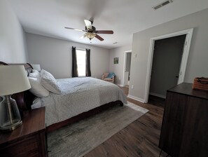 Ein Schlafzimmer mit einem Bett, einem Nachttisch, einer Lampe, einem Deckenventilator, einer Tür und einem Fenster.