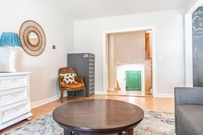A living room with a round coffee table, a wicker chair, a white dresser, and a patterned rug. - NEW! Pastry Townhouse - Steps to historic Southern Pines! (Southern Pines)