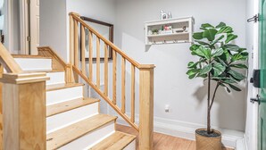 Un escalier avec des rampes et des marches en bois, une plante en pot et un mur blanc orné d’une étagère où sont exposés des objets décoratifs.