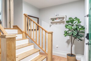 A staircase with wooden handrails and steps, a potted plant, and a white wall with a shelf displaying decorative items. - NEW! Pastry Townhouse - Steps to historic Southern Pines! (Southern Pines)