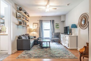 A living room with a sofa, a coffee table, a TV, and a decorative mirror. - NEW! Pastry Townhouse - Steps to historic Southern Pines! (Southern Pines)