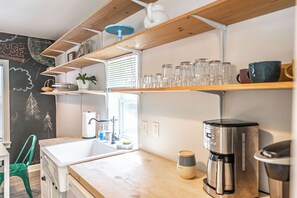 A kitchen with a wooden countertop, a coffee maker, and a shelf with glassware. - NEW! Pastry Townhouse - Steps to historic Southern Pines! (Southern Pines)