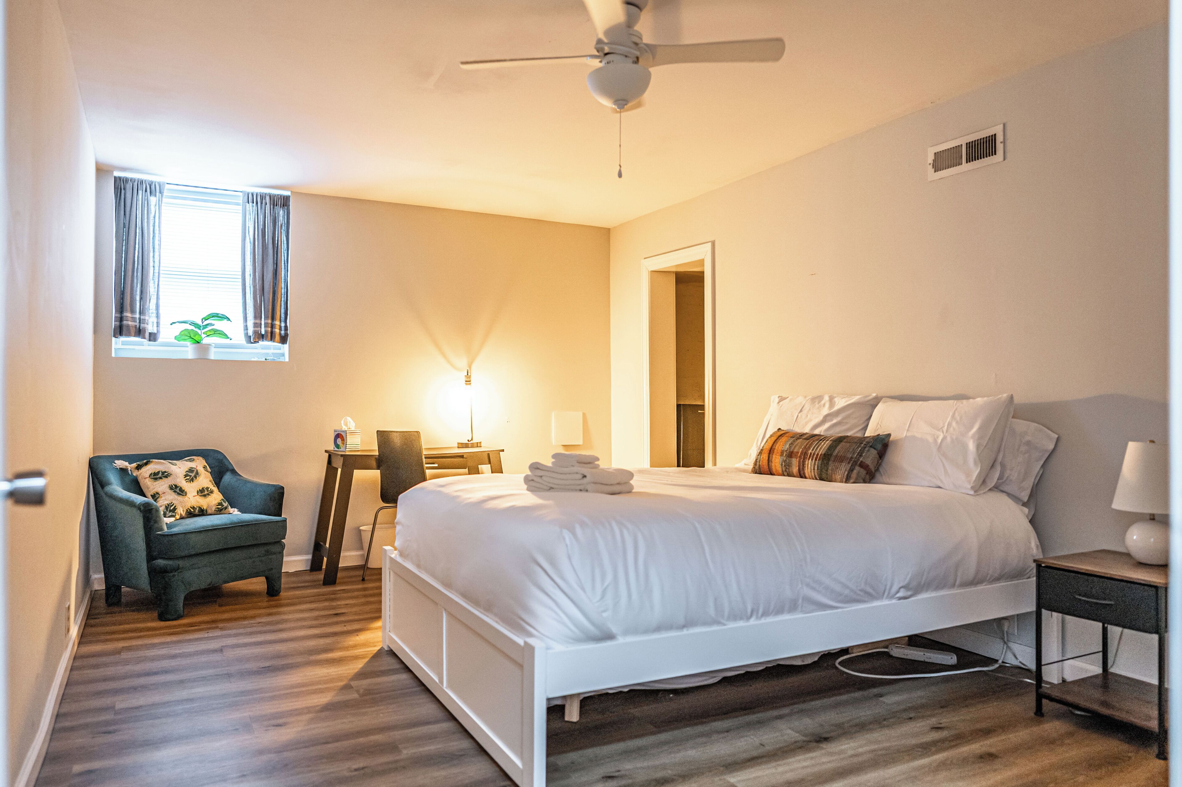 A hotel room with a bed, a chair, a desk, and a window with curtains.