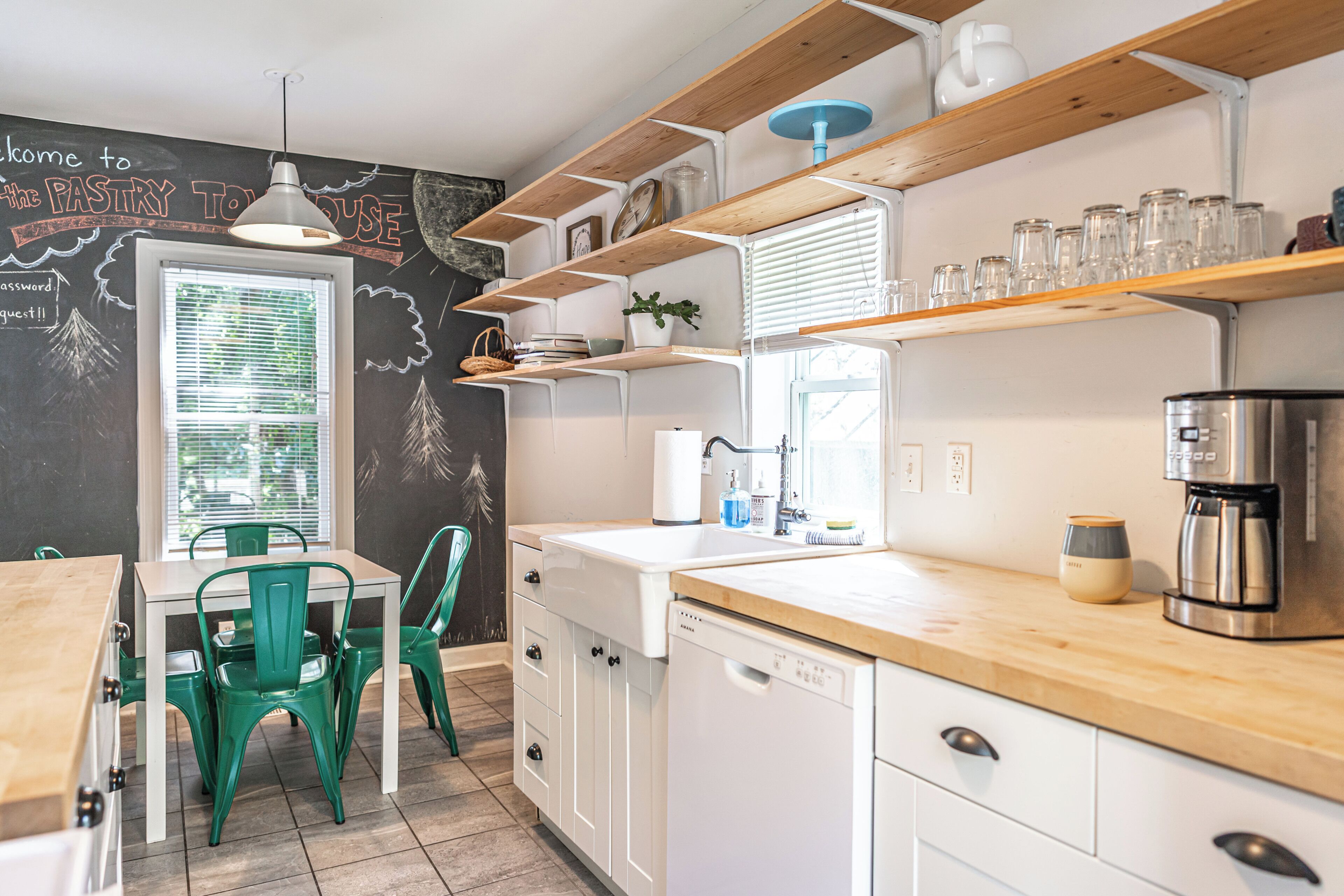 A kitchen with white cabinets, a coffee machine, and a chalkboard wall with writing.