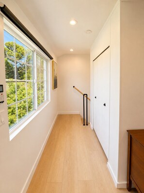 A hallway with a wooden floor, white walls, a window with a view of trees, and a door with a black handle. - Architectural Loft Home. Private Access with yard (La Cañada Flintridge)