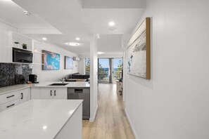 A modern kitchen with white cabinetry, a marble countertop, and a view to the outdoors. - One Bedroom Mediterranean Escape at Burleigh (Gold Coast)
