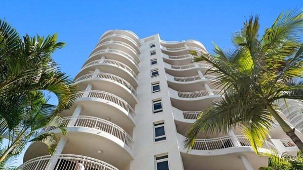 A multi-story hotel with balconies, palm trees, and a clear blue sky. - One Bedroom Mediterranean Escape at Burleigh (Gold Coast)