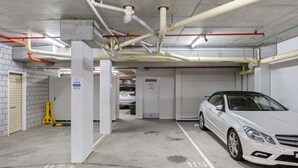 An underground parking garage with concrete pillars, white walls, and a white car parked in a designated space. - One Bedroom Mediterranean Escape at Burleigh (Gold Coast)