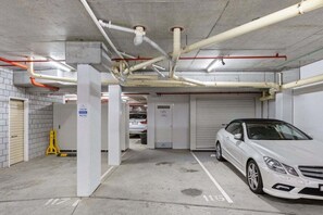 An underground parking garage with concrete pillars, white walls, and a white car parked in a designated space. - One Bedroom Mediterranean Escape at Burleigh (Gold Coast)