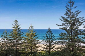 A coastal landscape with a clear sky, a sandy beach, and coniferous trees. - One Bedroom Mediterranean Escape at Burleigh (Gold Coast)