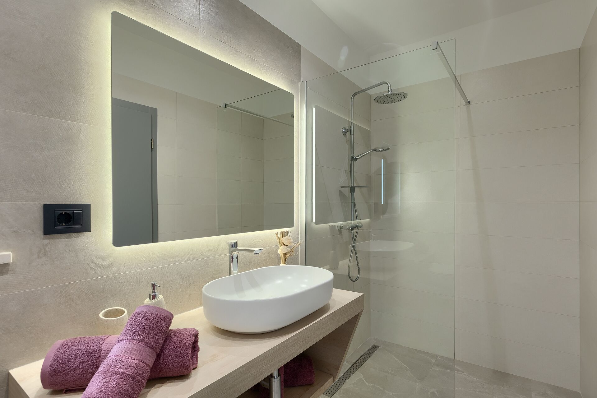 A modern bathroom with a large mirror, a white sink, and a glass-enclosed shower.