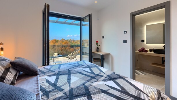 Et moderne soveværelse med en stor seng, en balkon med udsigt og et badeværelse med spejl og vask.