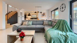 En moderne stue med en grå hjørnesofa, et sofabord med en potteplante og et grønt tæppe over sofaen.