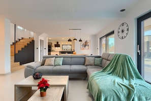 Ein modernes Wohnzimmer mit einem grauen Ecksofa, einem Couchtisch mit einer Topfpflanze und einer grünen Decke, die lässig über die Couch gelegt ist.