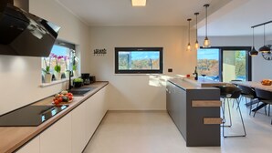 Et moderne køkken med en central ø, indbygget ovn og et vindue med udsigt til et smukt landskab.