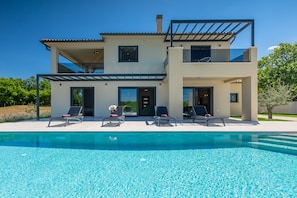 Ein zweistöckiges Haus mit Swimmingpool, Sitzgelegenheiten im Freien und einer Pergola.