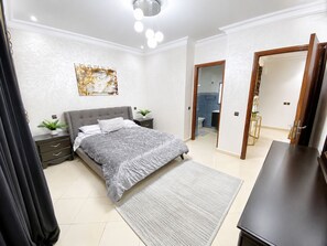 A bedroom with a bed, bedside tables, a painting, and a bathroom visible through an open door. - Big 4-bedroom apartment with AC in Center Kénitra next to TGV train (Kénitra)
