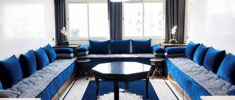 Un salon moderne avec un grand canapé d’angle, une table basse ronde et un tapis décoratif.