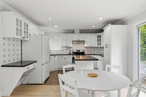 A modern kitchen with white cabinetry, a central island, and a dining table with chairs. - 4BR Family Retreat in Surrey (Surrey)