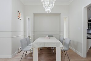 Ein Essbereich mit einem weißen Tisch, zwei grauen Stühlen, einer Pendelleuchte und einem gerahmten Bild an der Wand.