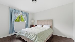 Une chambre à coucher avec un lit, une table de chevet, une lampe et une fenêtre avec des rideaux.