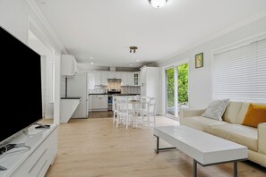 A modern living room with a flat-screen TV, a white sofa with yellow pillows, and a dining area with white chairs. - 4BR Family Retreat in Surrey (Surrey)