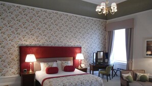 Habitación de hotel con una cama grande, dos mesitas de noche con lámparas, un escritorio, una silla y un sofá.