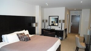 Habitación de hotel con una cama grande, un escritorio, una silla, un espejo y una puerta que da a otra habitación.