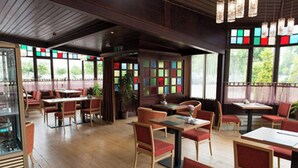 Interior de restaurante con suelos de madera, mesas, sillas y amplios ventanales con vidrios de colores.