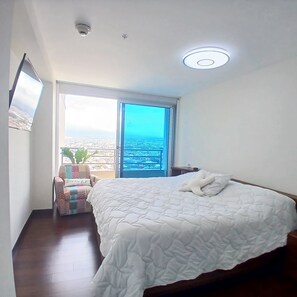 Ein Schlafzimmer mit einem großen Bett, einem Fenster mit Blick auf die Stadt und einer Deckenleuchte.