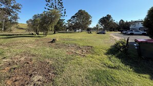 A grassy area with trees, a white building, and parked vehicles. - Five Mile Motel (South Grafton)