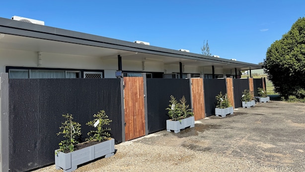 A row of modern hotel rooms with dark exterior walls, wooden doors, and small potted plants in front. - Five Mile Motel (South Grafton)