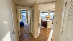 A hallway leading to a bedroom with a city view, a kitchen with a large window, and a dining area with a vase of flowers. - Shaw 2BR Penthouse | Monument Views, Balconies & Rooftop (washington)
