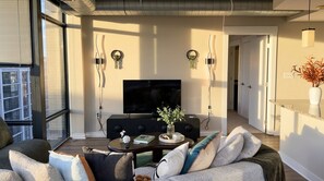 A modern living room with a flat-screen TV, a coffee table with decorative items, and a sofa with cushions. - Shaw 2BR Penthouse | Monument Views, Balconies & Rooftop (washington)