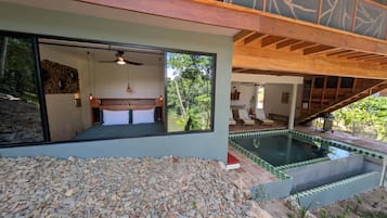 A modern bedroom with a large bed, a ceiling fan, and a view of a swimming pool.
